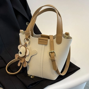Bucket Bag aus Leder in Cremeweiß und Braun mit Bärenanhänger auf schwarzem Anzug