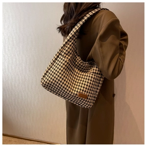 Detail of houndstooth knit tote bag with leather logo tag worn by a model
