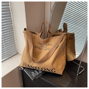 Detail view of large brown canvas tote bag featuring adjustable strap and letter print