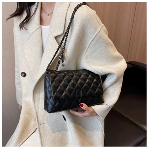 Close-up of black quilted chain bag with unique metal buckle on a white coat background