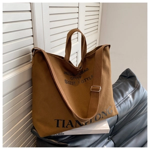 Detail of a large brown canvas tote bag featuring dual handles and adjustable shoulder strap