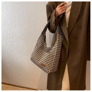 Detail of houndstooth tote bag featuring a brown leather logo patch on the fabric
