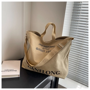 Detail of high-capacity canvas tote bag with lettering, top handle, and crossbody strap