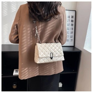 Close-up of a white quilted chain bag worn by a model in a minimalist stylish indoor setting