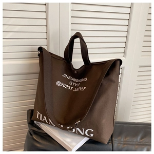 Detail of a large brown canvas tote bag with white lettering and sturdy handles