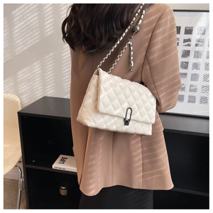Close-up of cream quilted chain bag with elegant black metal lock and woven strap