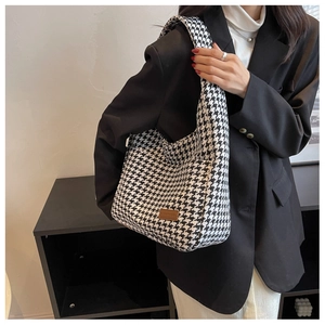 Detail of black and white houndstooth tote bag with brown leather patch and wide strap