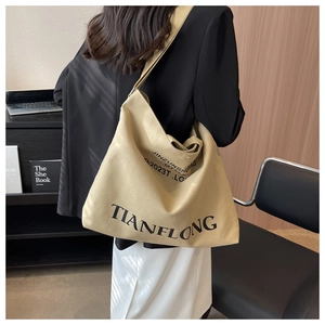 Detail view of a large beige canvas tote bag with black lettering on a shoulder strap