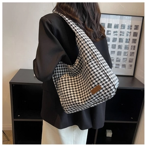 Detail of a large houndstooth tote bag with a brown leather label shown on a shoulder