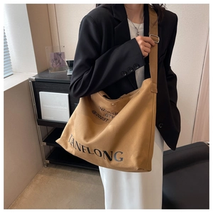 Model wearing a large khaki canvas tote bag featuring adjustable strap and black lettering