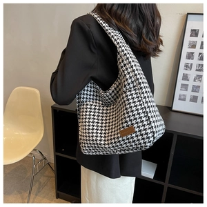Side view of a large houndstooth knit tote bag with leather tag detail on female model