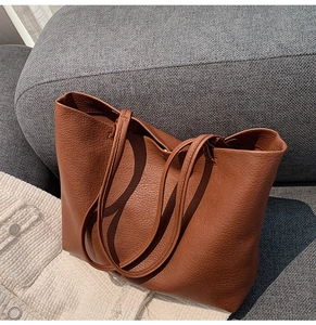 Detailed close-up of brown litchi pattern leather tote bag on a textured sofa background