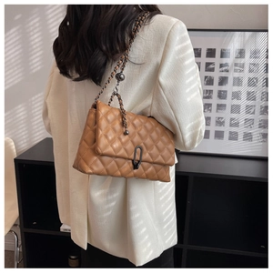 Detail of a brown quilted leather crossbody bag with metal chain strap on model shoulder