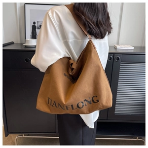 Detailed view of a brown canvas tote bag with a wide strap shown on a model
