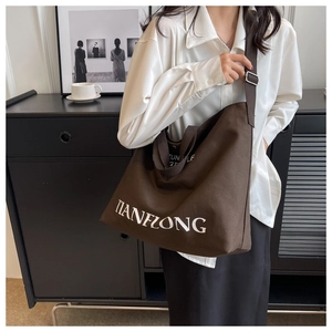 Detail of adjustable wide shoulder strap on a large canvas tote with white lettering
