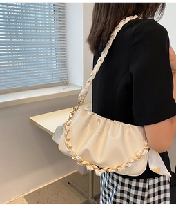 Detail van de crèmekleurige cloud bag met geweven riem en zijden ketting met hartjes