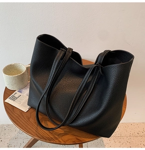 Detailed view of black pebbled leather tote bag texture on a dark wooden table