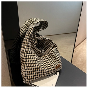 Close-up of houndstooth tote bag with brown leather logo patch on a textured tweed fabric