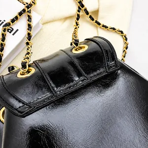 Détail du cuir brillant noir avec coutures fines et chaîne dorée sur un sac de luxe