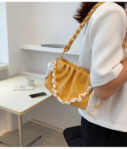 Detail van gele geplooide cloud bag met hart sjaal ketting en geweven schouderriem