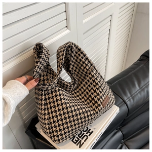 Close-up of houndstooth tote bag with brown leather logo tag on artistic books