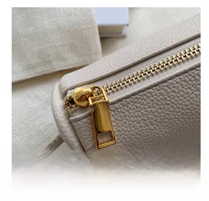 Detail of smooth gold zipper and white litchi grain leather on a saddle bag