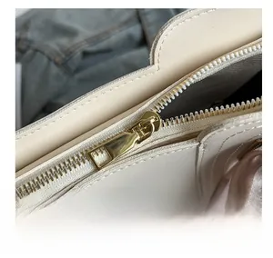 Close-up of smooth golden metal zipper and cream leather texture on the tote bag