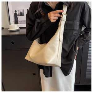 Close-up of a cream-colored half-moon shoulder bag with adjustable strap and metal buckle