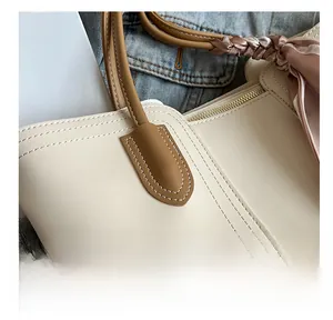 Detail shot of cream tote bag featuring reinforced brown handles with a floral scarf accent