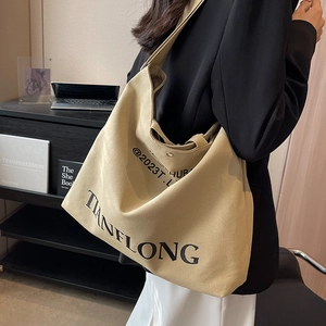 Large khaki canvas tote bag with black typography print and wide shoulder strap