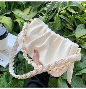 Detail van de crèmekleurige plissé cloud bag met geweven handvat en zijden sjaalketting