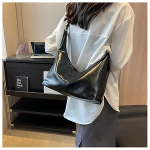 Detail of a black high-shine large hobo bag worn as a shoulder bag for commute