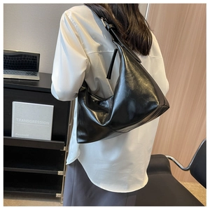 Macro side view of a minimalist black leather hobo bag with a wide shoulder strap