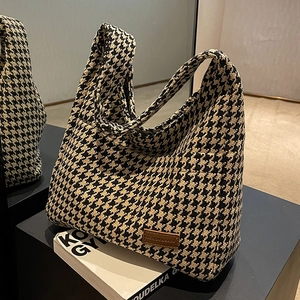 Classic black and white houndstooth tote bag with brown leather tag on geometric stand
