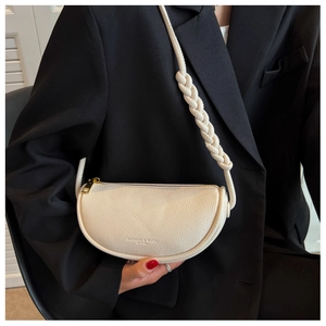 Close-up of cream textured leather saddle bag with woven shoulder strap detail