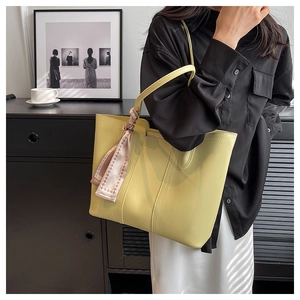 Detail of light yellow tote bag featuring a decorative fashion scarf on the handle