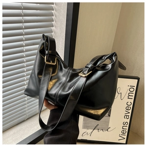 Close-up of black glossy leather shoulder bag featuring adjustable golden metal buckle detail