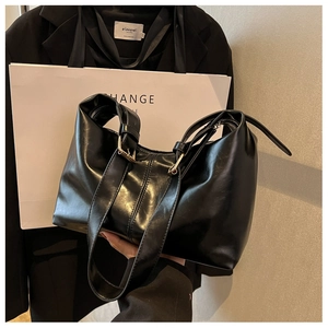 Close-up of black glossy leather dumpling bag with golden metal buckle and wide strap