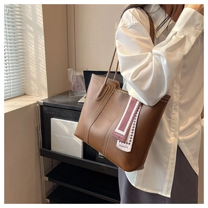 Detailed side view of a brown tote bag with white stitching and a pink silk scarf accessory