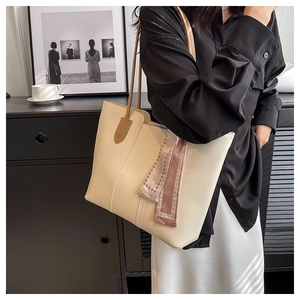 Detail of a large off-white tote bag with brown leather handles and a fashion silk scarf