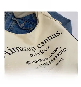 Detailed macro view of beige canvas tote bag with black letter print and denim fabric