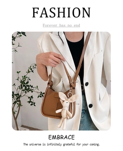 Caramel leather saddle bag with cute rabbit pendant shown on a model in white blazer
