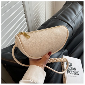 Detail of cream saddle bag with lychee texture and woven handle on leather sofa