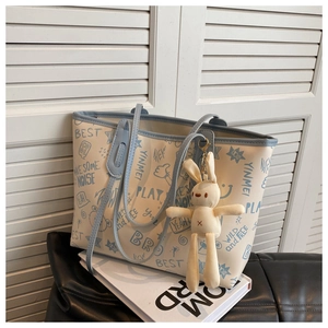 Macro detail of graffiti tote bag showing printed text, charms, and light blue strap finish