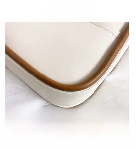 Close-up of white leather shoulder bag with brown piping and detailed stitching
