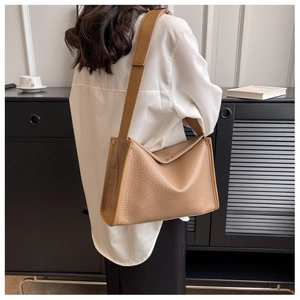Dettaglio della borsa tote in pelle marrone con motivo litchi e tracolla larga su modella