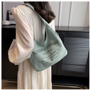 Detail of light green canvas tote bag showing wide shoulder strap and black lettering