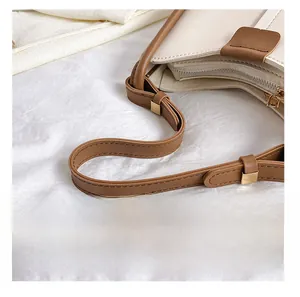 Close-up of the brown leather shoulder strap with a gold metal buckle on a beige handbag