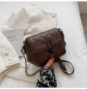 Détail d'un sac matelassé marron avec boucle ovale noire sur un tissu en tweed