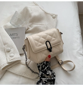Détail d'un sac à rabat matelassé beige avec chaîne argentée et boucle noire en U